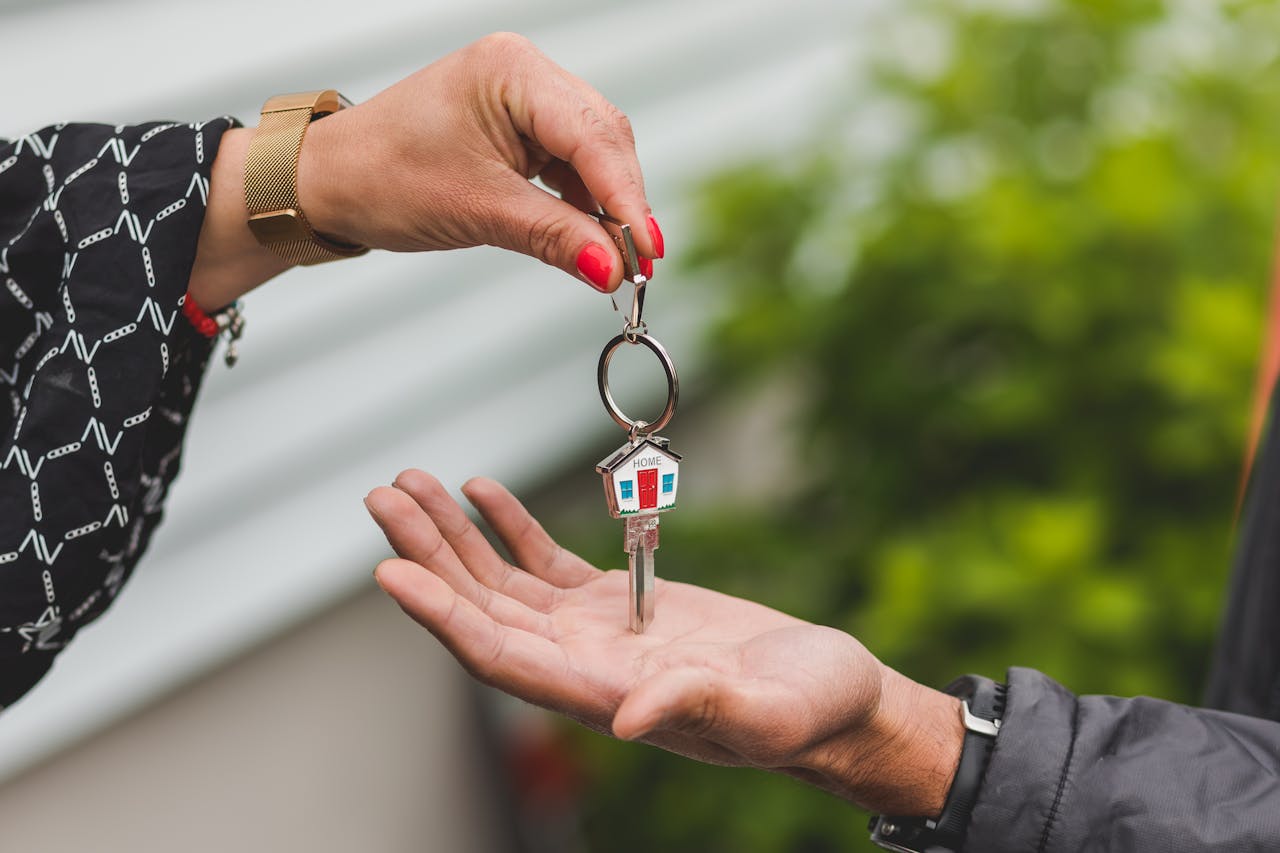 How a good project manager makes a big difference for home construction Close-up of a hand handing over a key with a house keychain, symbolizing real estate transaction.